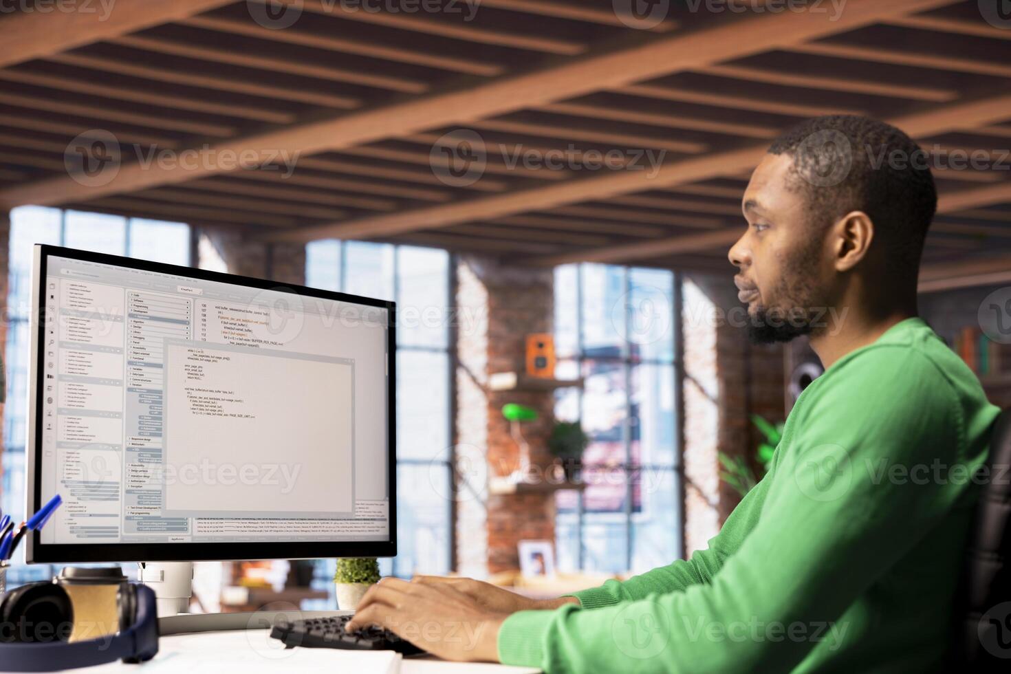 Man in home office looking at UI on PC screen, typing and executing programming code. Coding application UI used by african american IT developer writing and testing code in modern apartment photo