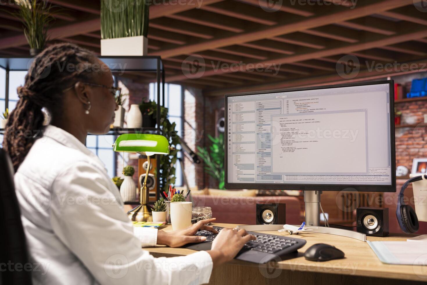Woman in home office looking at UI on computer screen, typing and executing programming code. Coding application UI used by african american IT developer writing and testing code in modern apartment photo