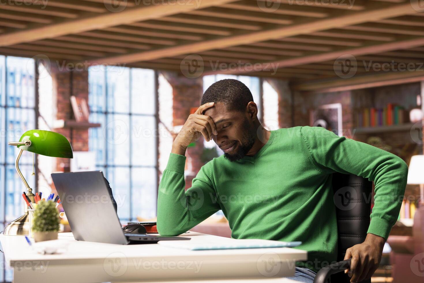 Remote employee at home office desk waiting for laptop operating system to open, feeling bored. Impatient african american man frustrated by long wait time while using software on notebook photo