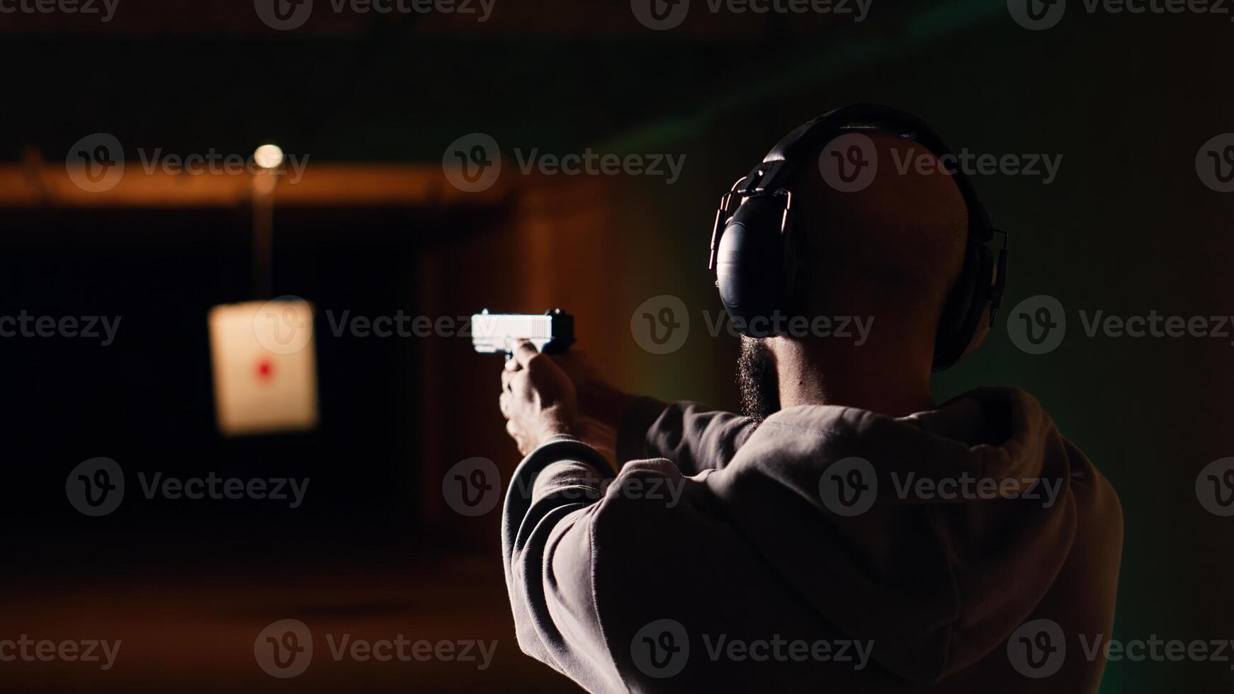 Person wearing protecting gear loading magazine in pistol during firearm practice session at shooting range. Gun enthusiast reloading handgun, learning self defense, pointing weapon, camera B photo