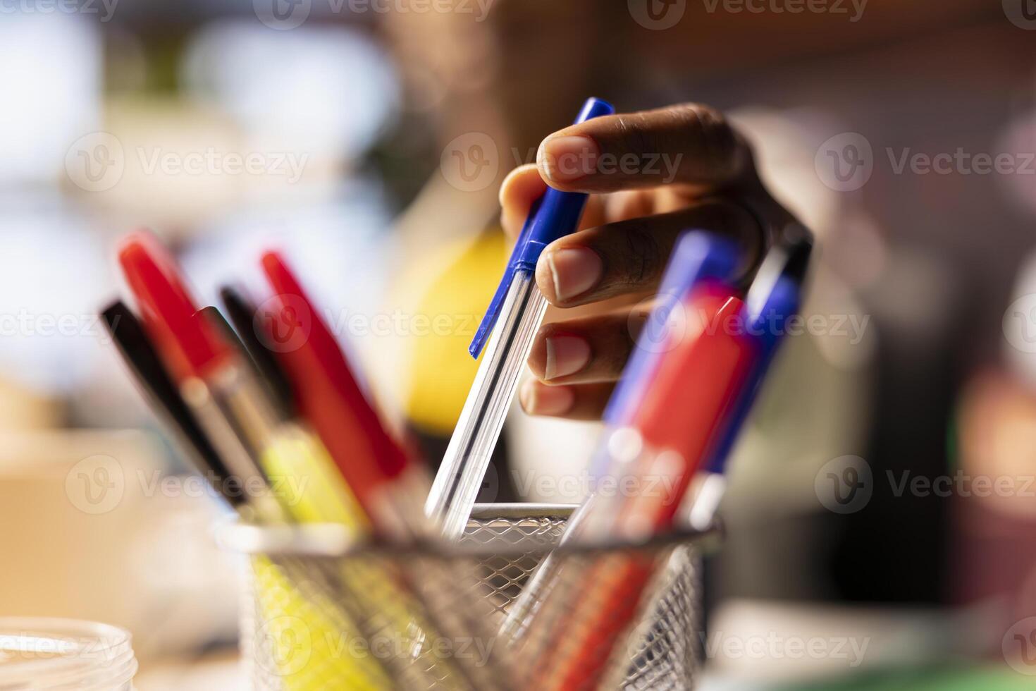 Extreme close up of pen taken by person from desk organizer to annotate document. Focus on workspace stationary holder used by student in blurry background requiring writing tool photo