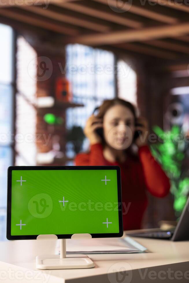 Casual person joining virtual workshop online next to chroma key screen, uses headset during the lesson on a website. Focused woman on virtual network connection, multitasking at home. photo