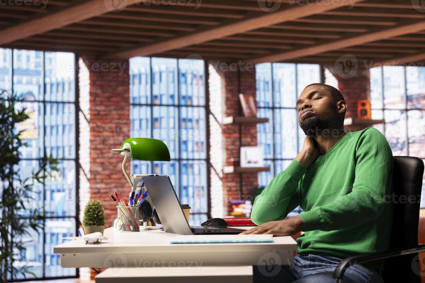 Tired man with eyes closed at desk in apartment feeling exhausted after sleepless night. African american person being sleepy during morning, awaken too early, showing sleepiness photo