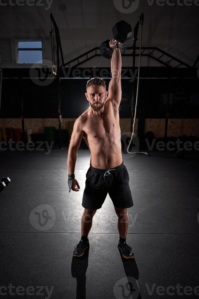 Strong sportsman doing exercises with dumbbell in gym photo