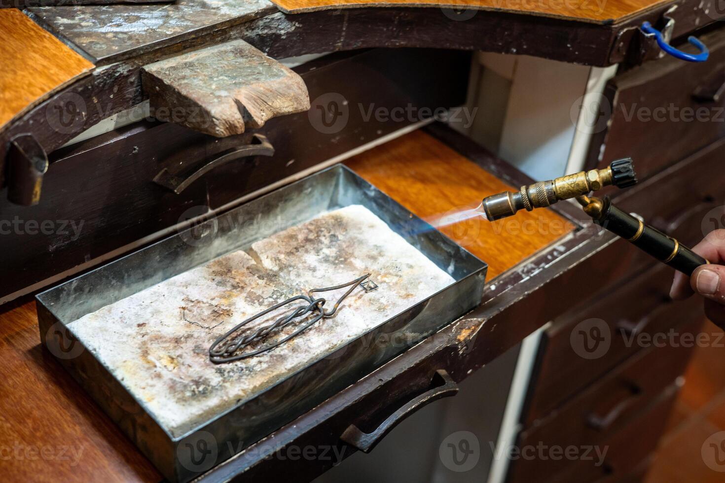 Jeweler melting silver metal with open flame blow torch welding. Goldsmith working and creating in his jewelry workshop. photo