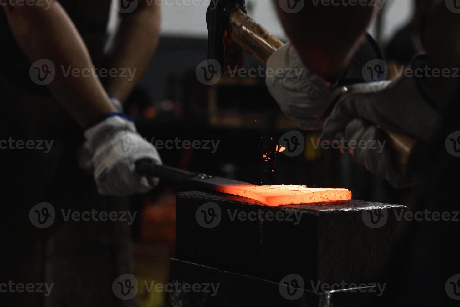 Blacksmiths forging hot metal with hammer in workshop photo