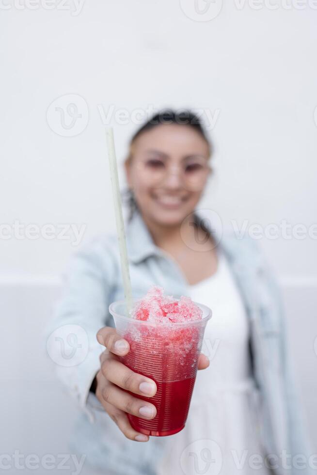 A young Hispanic woman is smiling while drinking a Mexican cherry slushy outdoors photo