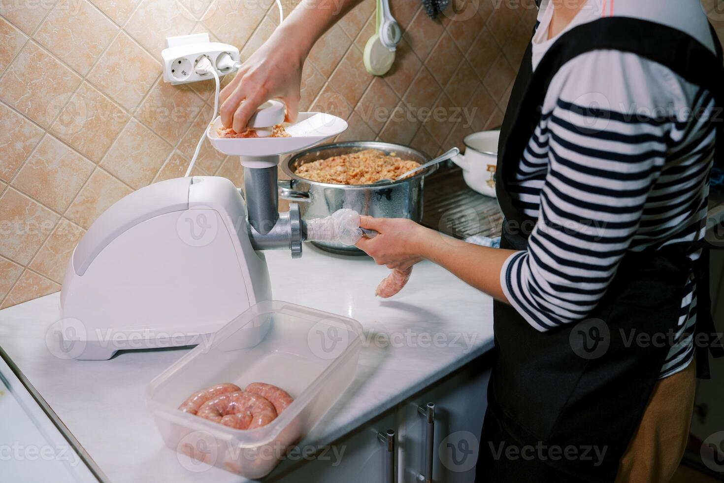 Chef stuffs the gut with minced meat on an electric meat grinder, pushing it with a pusher in the tray photo