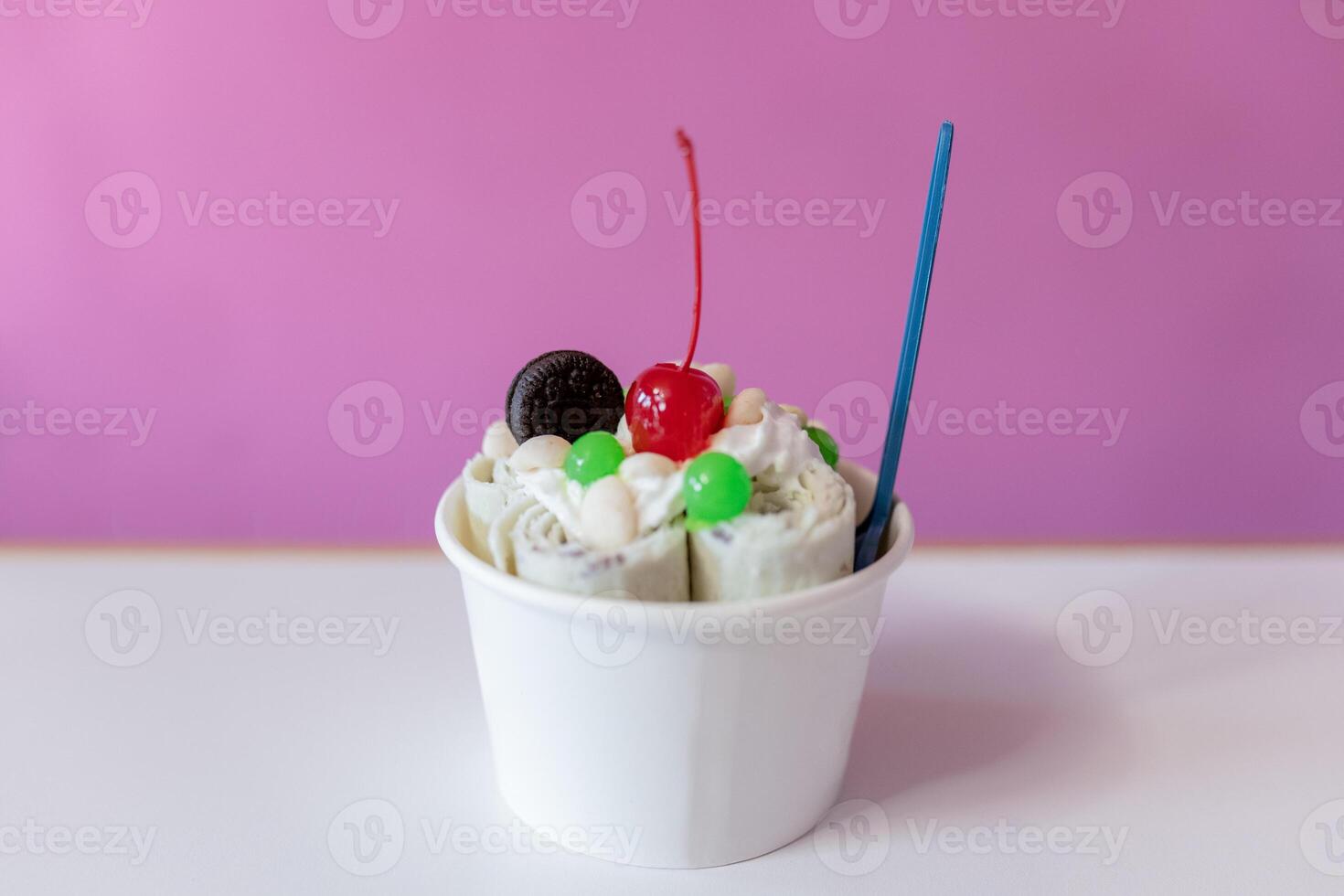 Close up of a rolled ice cream decorated with a cherry, a cookie and green bubble toppings photo