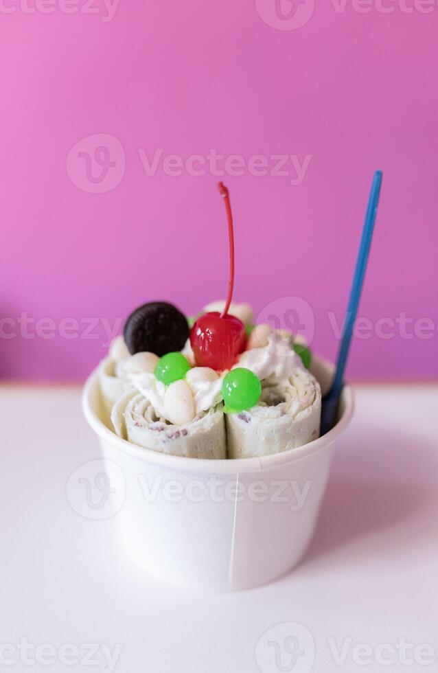 Close up of a rolled ice cream decorated with a cherry, a cookie and green bubble toppings photo
