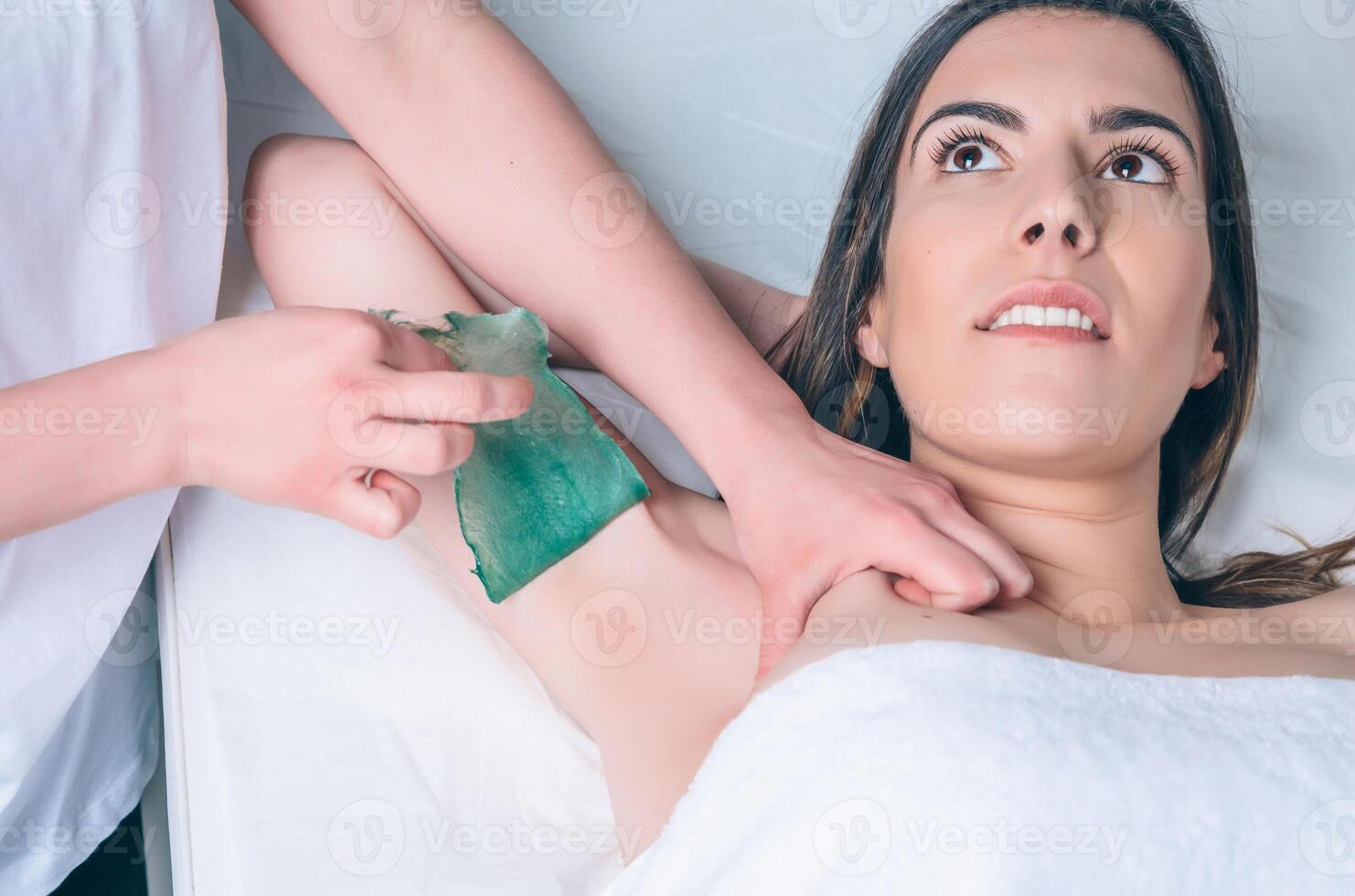 Beautician hands doing depilation in woman armpit with wax strip photo