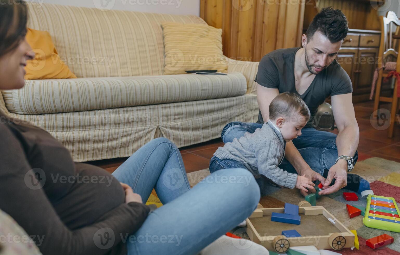 Father playing with toddler while the mother is looking at them photo
