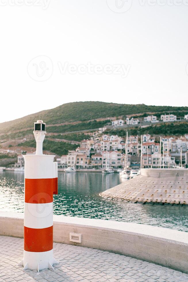 Small striped red and white lighthouse stands on a pier by the sea photo