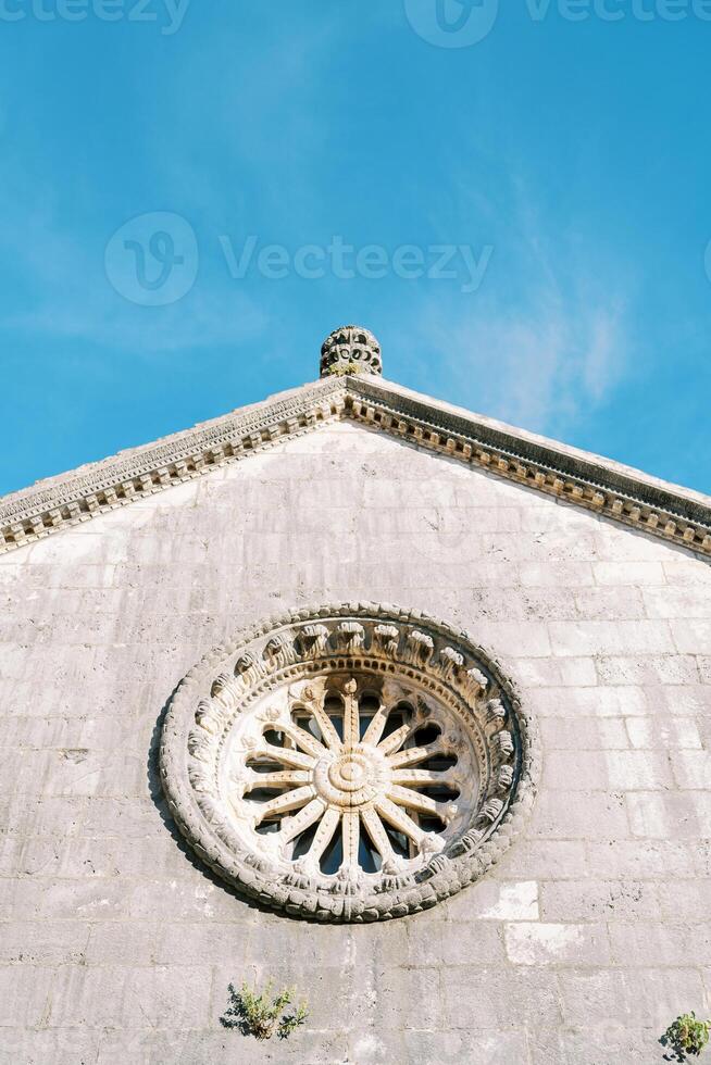 Rose window on the facade of an ancient stone church against a blue sky photo