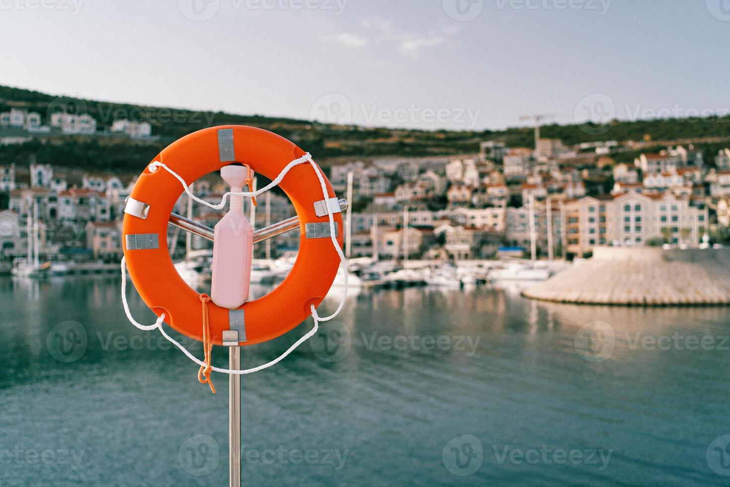 Lifebuoy on a steel post with a lock by the sea against the backdrop of colorful houses on the coast photo