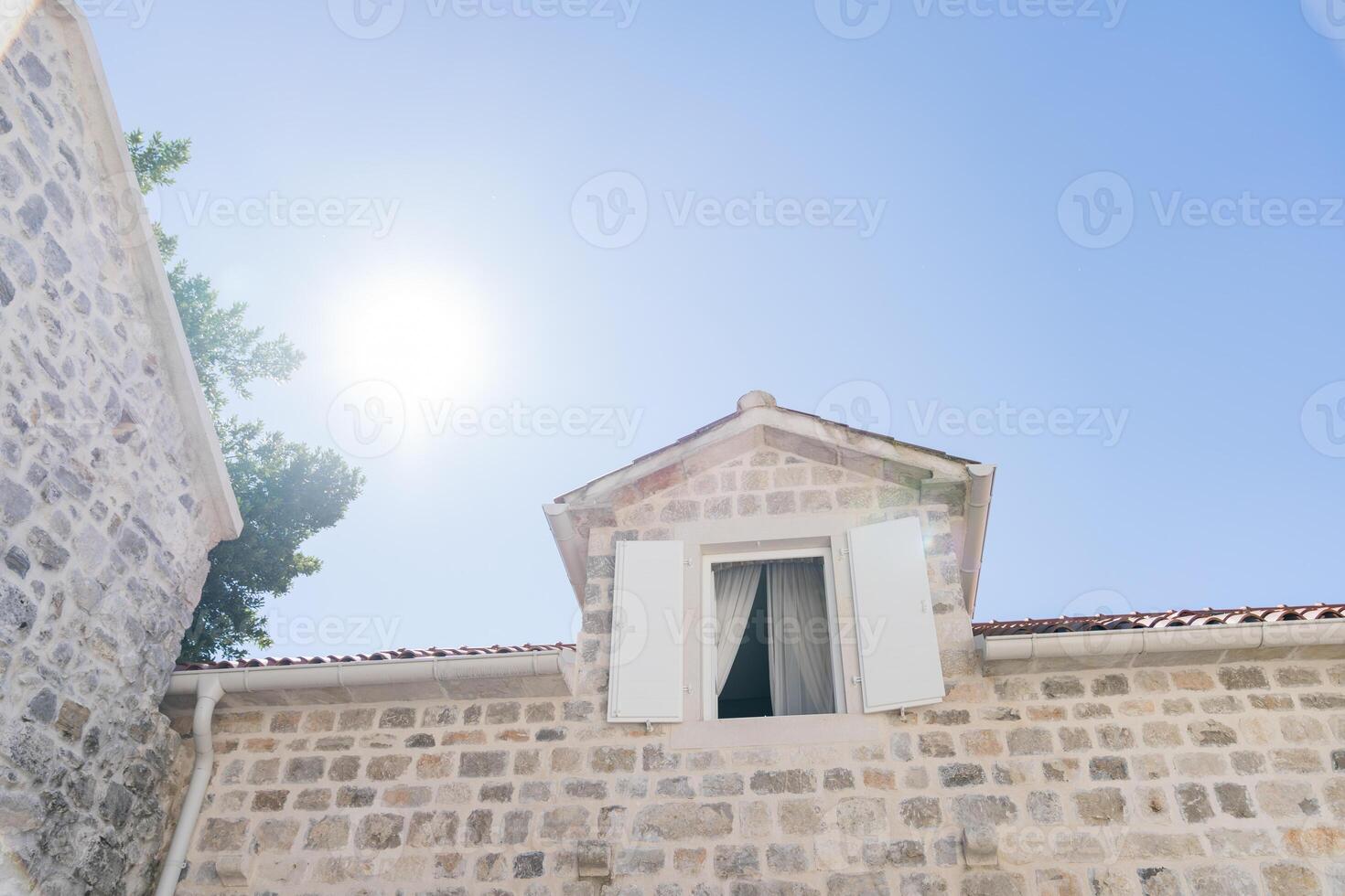 Open shutters in the attic of an old stone house against a background of sunny blue sky photo