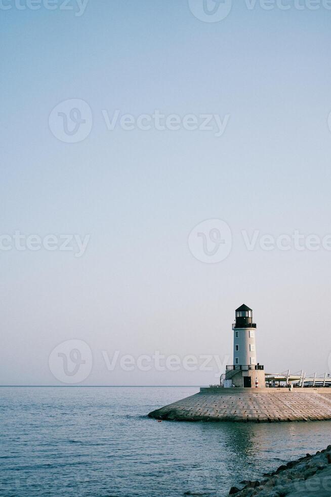 White lighthouse on a breakwater by the sea against a blue sky photo