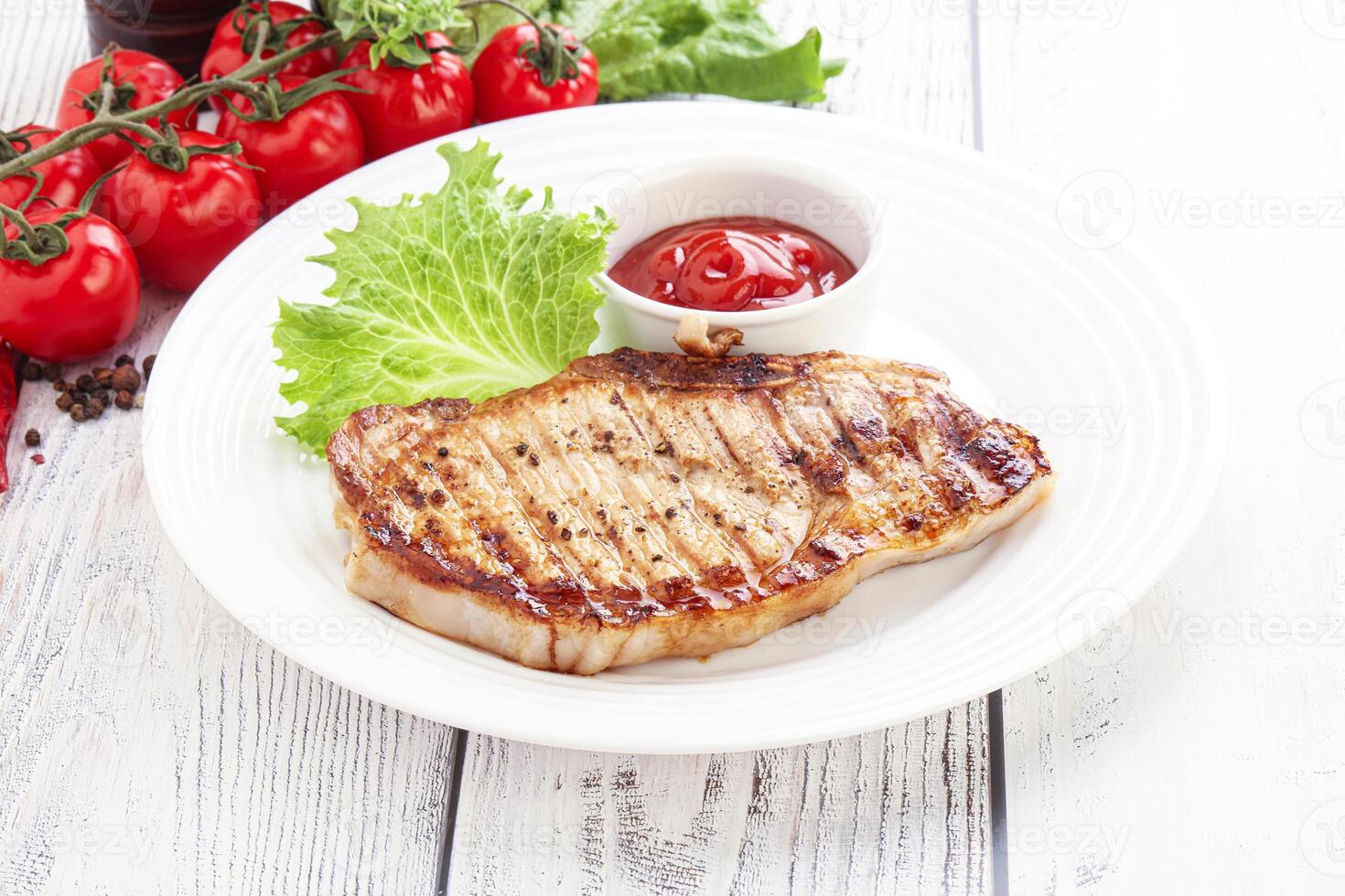 Grilled pork steak with tomato sauce and lettuce on white plate photo