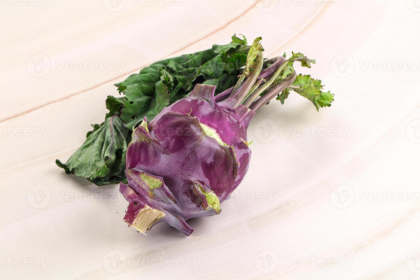 A purple vegetable with green leaves sitting on a white surface photo