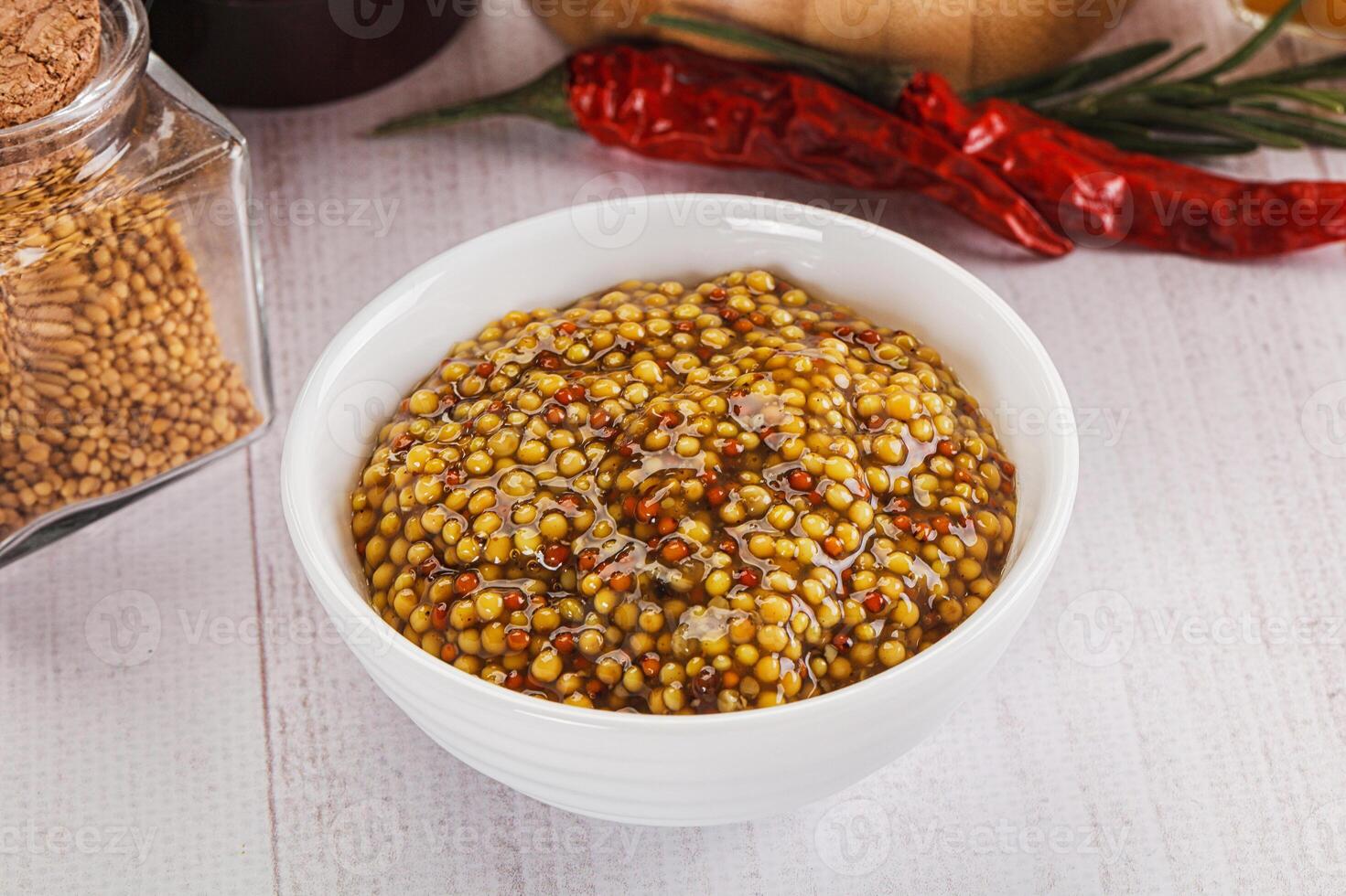 A bowl of mustard and spices next to a jar of chili photo