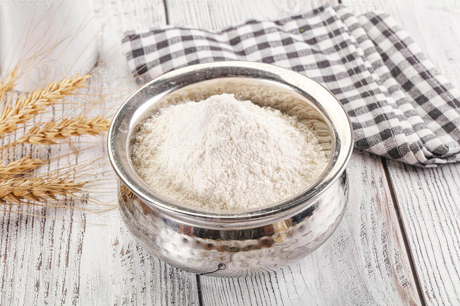A bowl of flour and a spoon next to a glass of milk photo