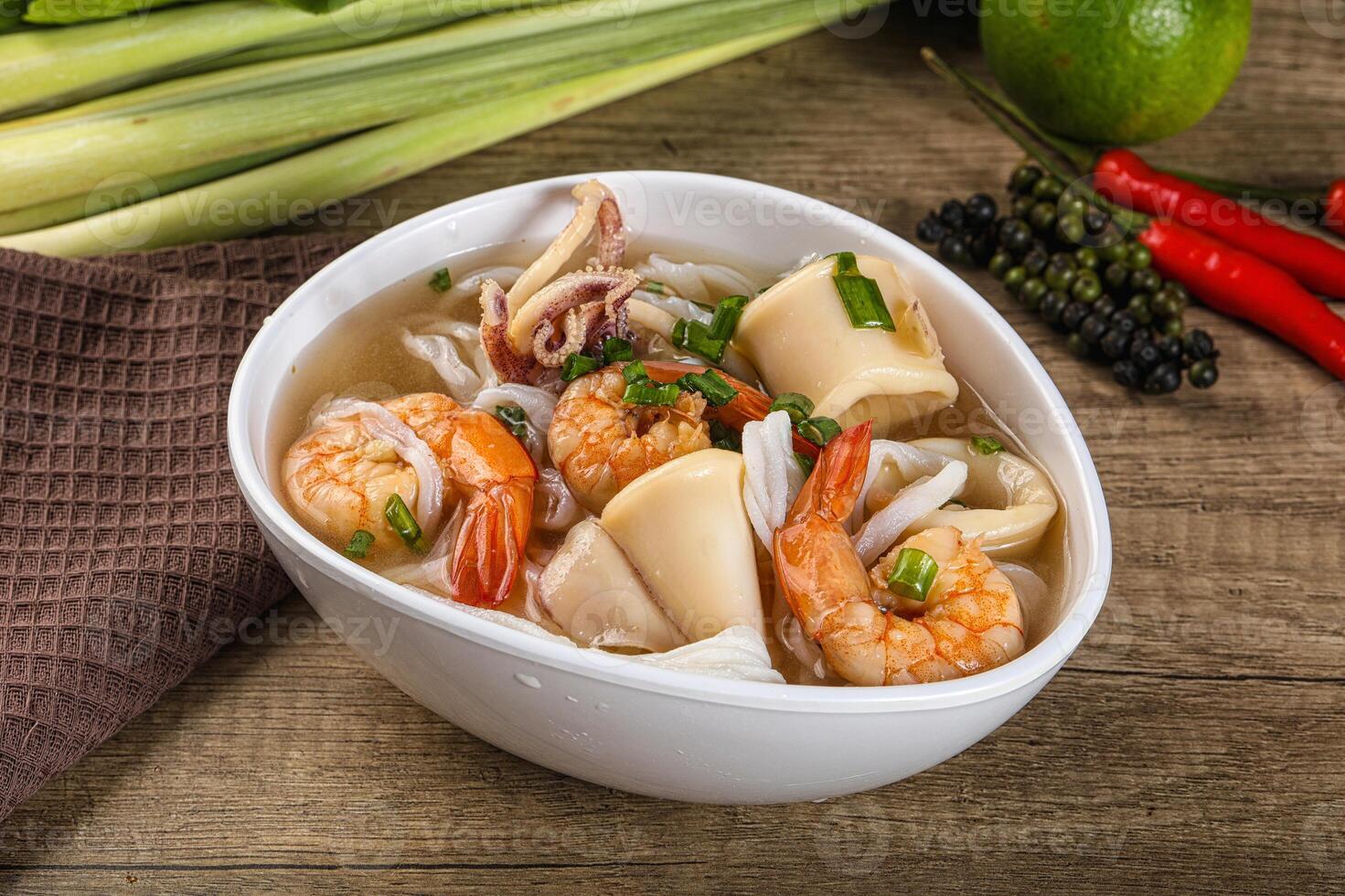A bowl of soup with shrimp and vegetables on a table photo
