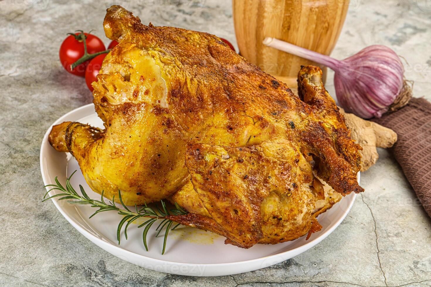 A large roasted chicken on a plate with a side of vegetables photo