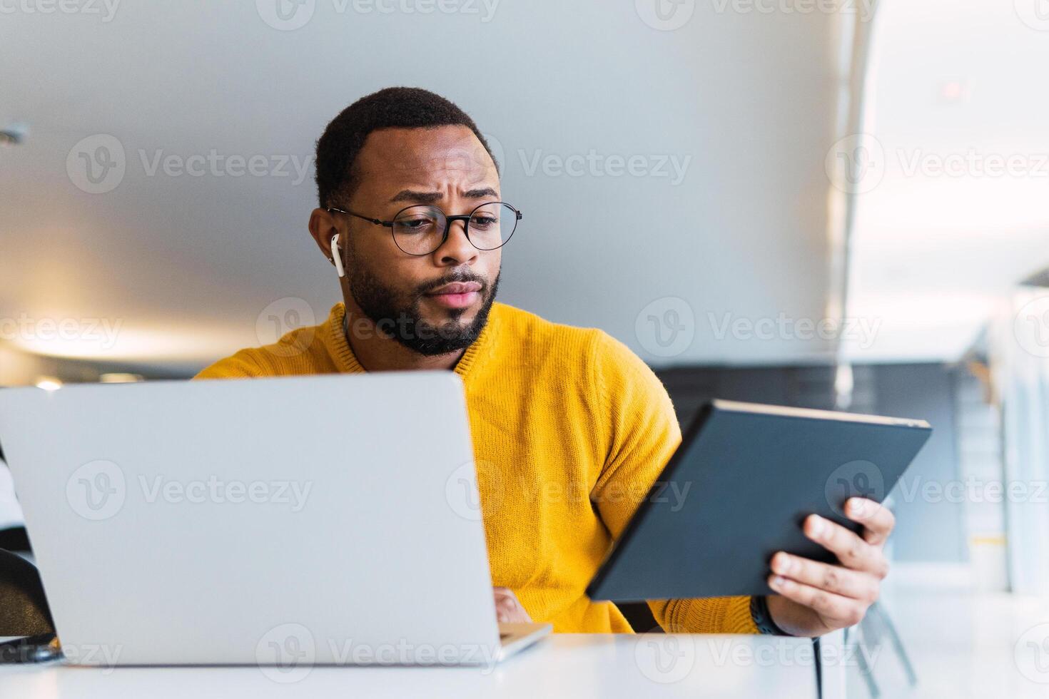 Man with earbuds using tablet and laptop at table photo