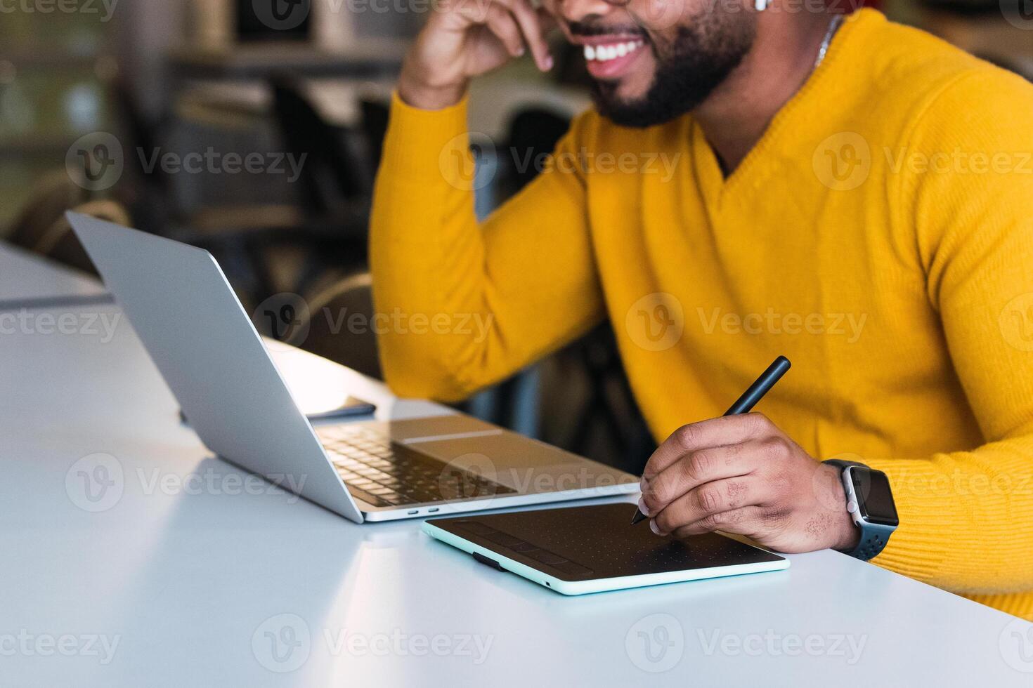 Anonymous smiling black man working on laptop with tablet photo