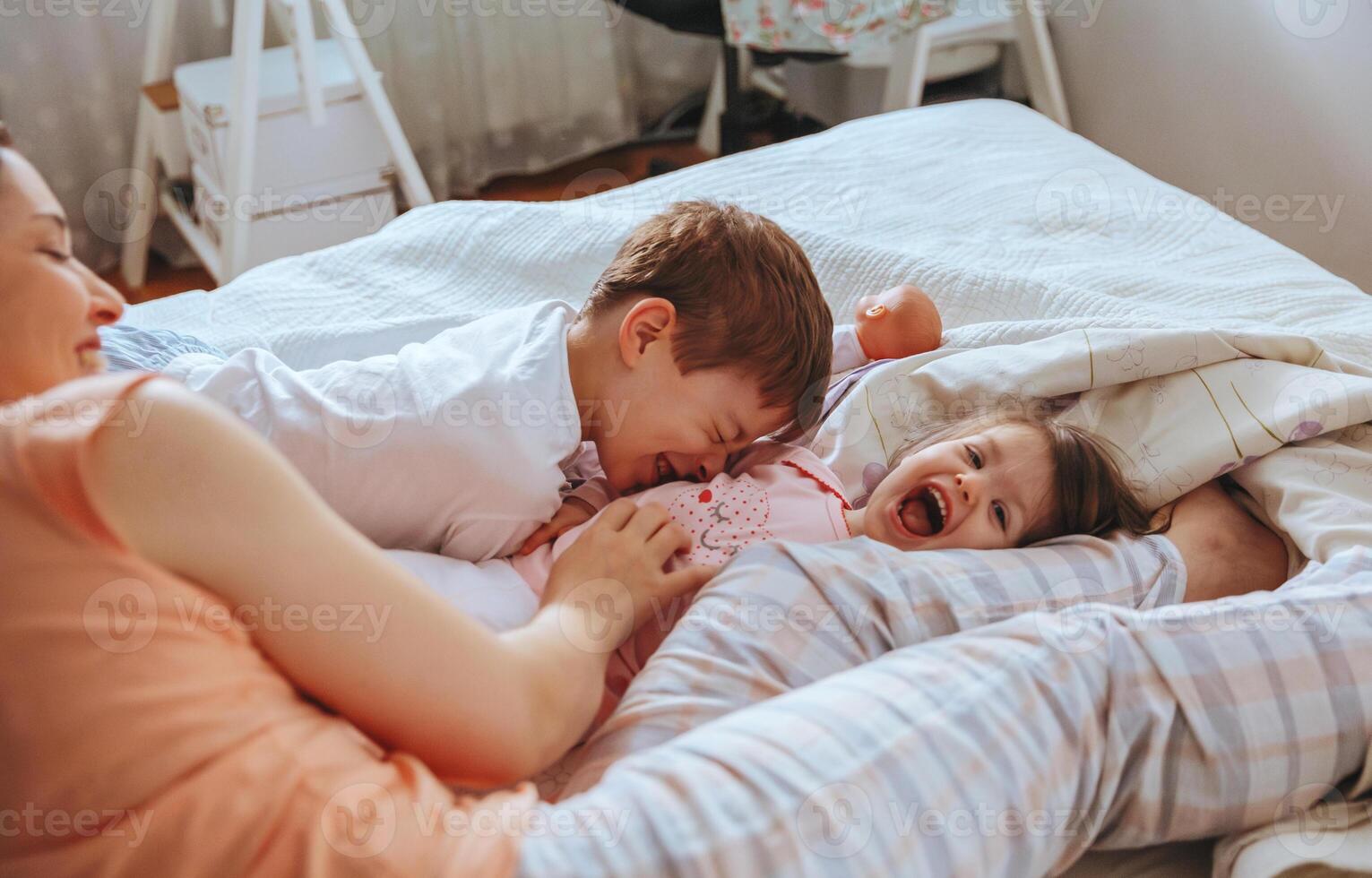 Relaxed mother and sons playing over the bed photo
