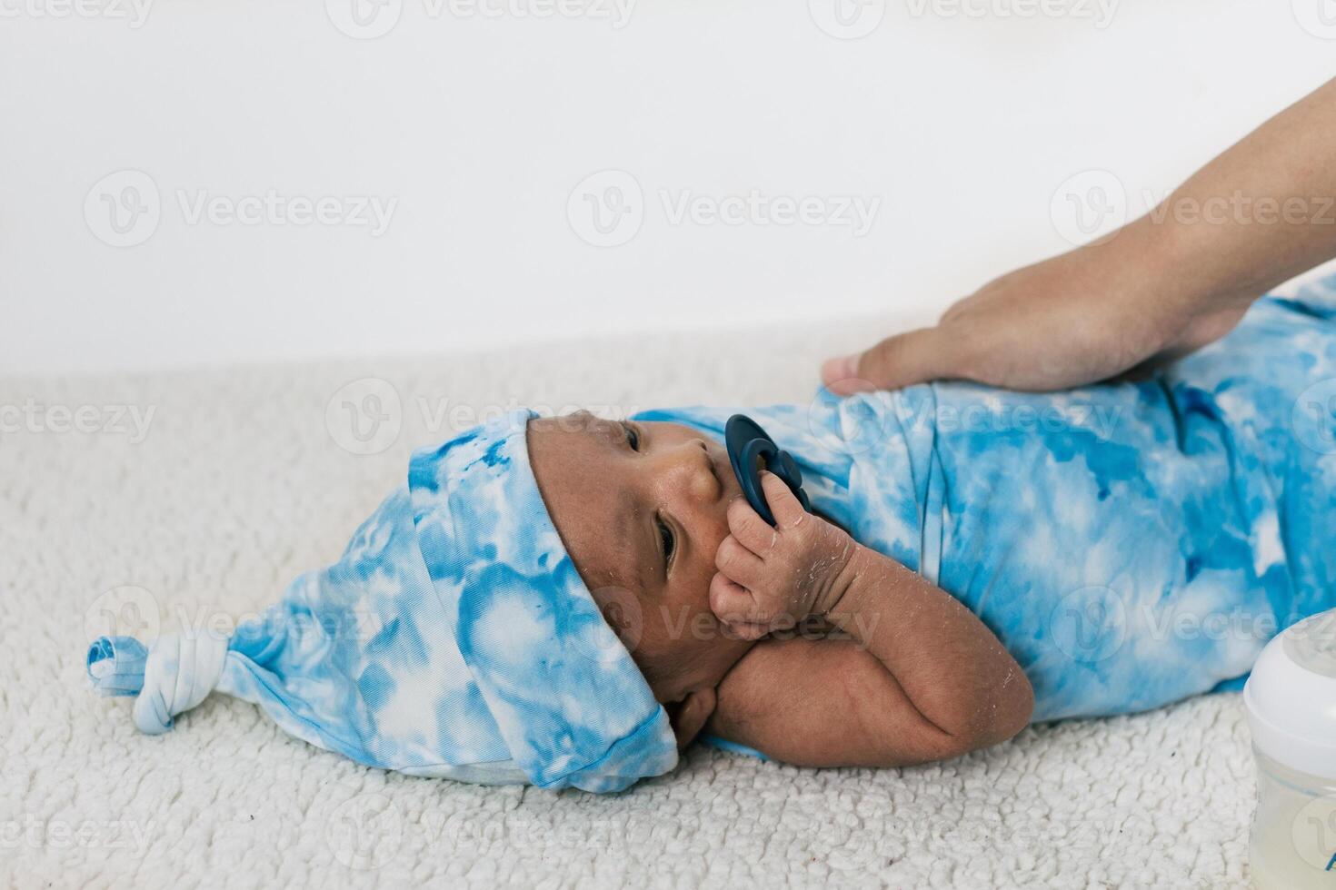 Anonymous mother with newborn baby wrapped on soft blanket with pacifier photo