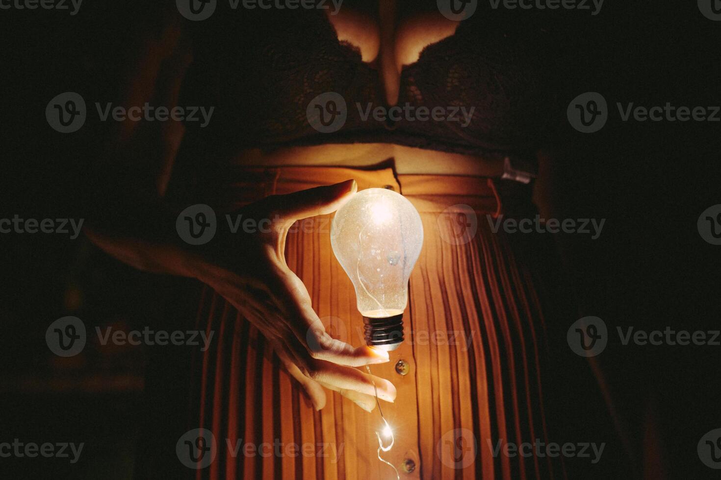 Faceless female with lightbulb in darkness photo