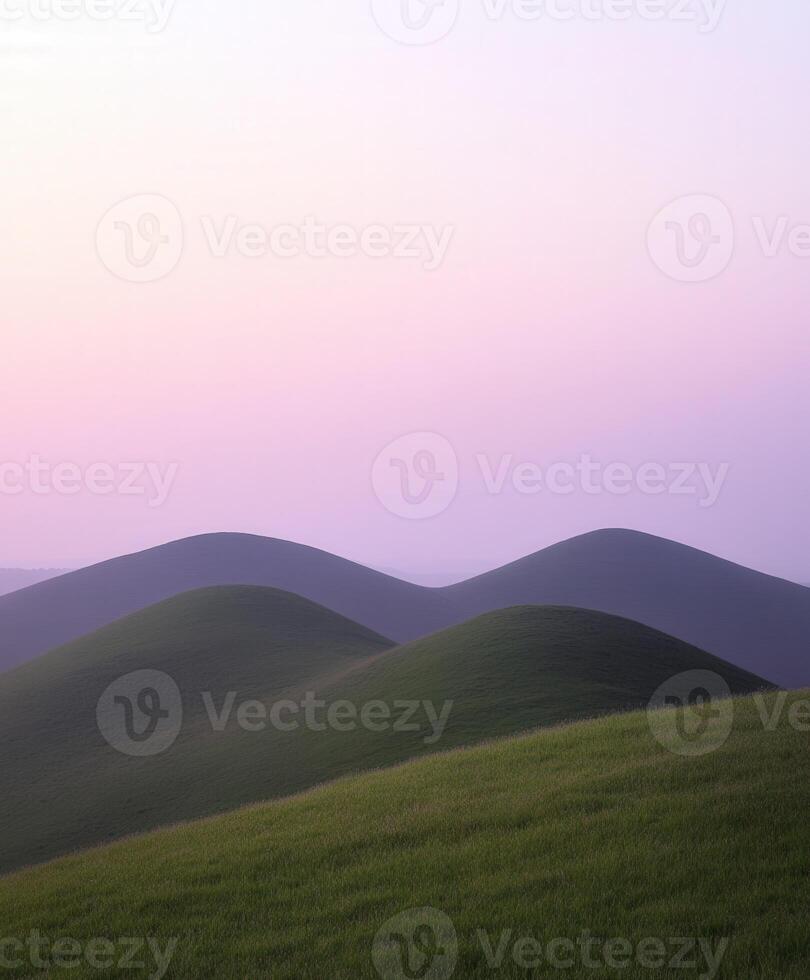 A grassy hill with a pink sky and hills photo
