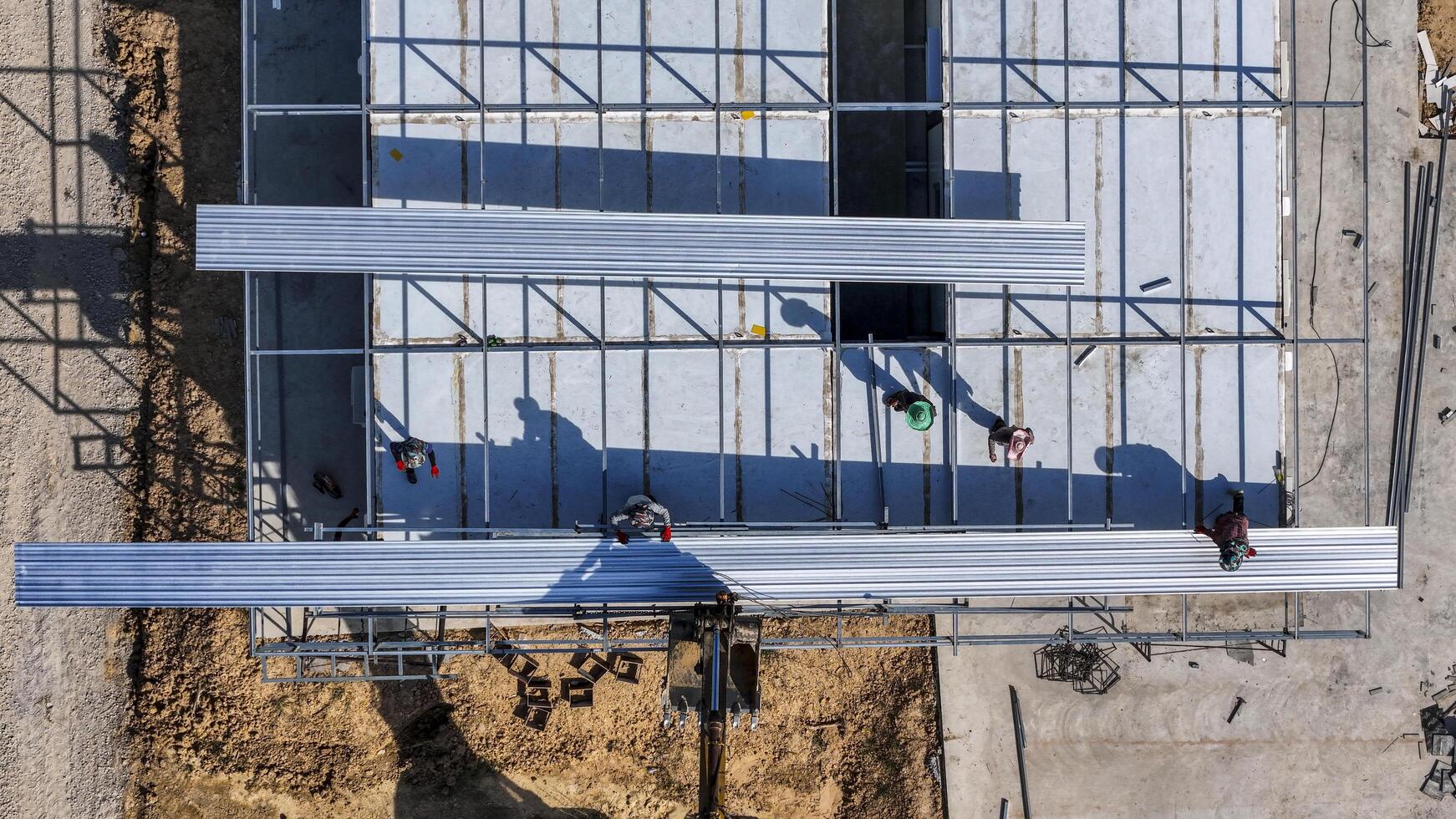 Aerial view of workers placing long metal sheets onto a building framework with the aid of heavy machinery, highlighting precision, teamwork, and modern techniques in construction projects photo