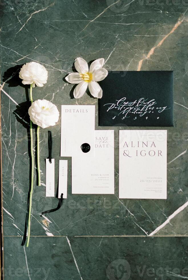 Wedding invitations lie next to name tags and flowers on a green marble table photo