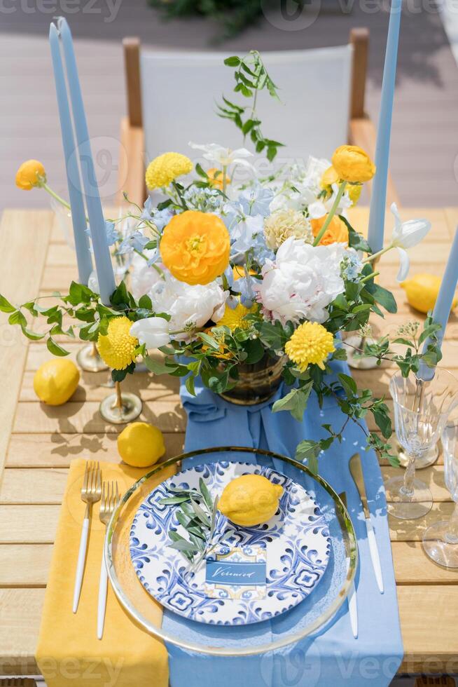 Name card lies next to an olive branch and a lemon on a plate on a set table near a colorful bouquet of flowers photo