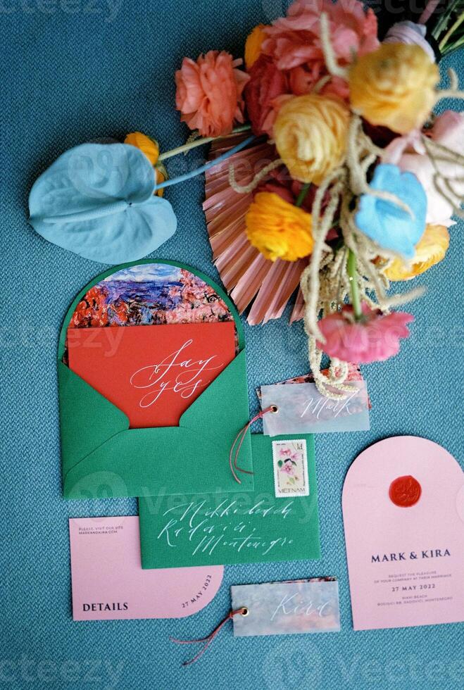Wedding invitations with name cards, green envelopes and a bouquet of flowers lie on a blue sofa photo