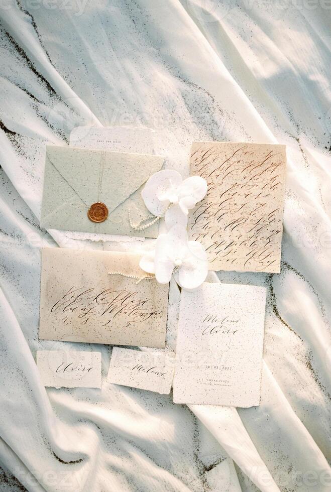 Wedding invitations and name cards lie on a white cloth sprinkled with sand photo