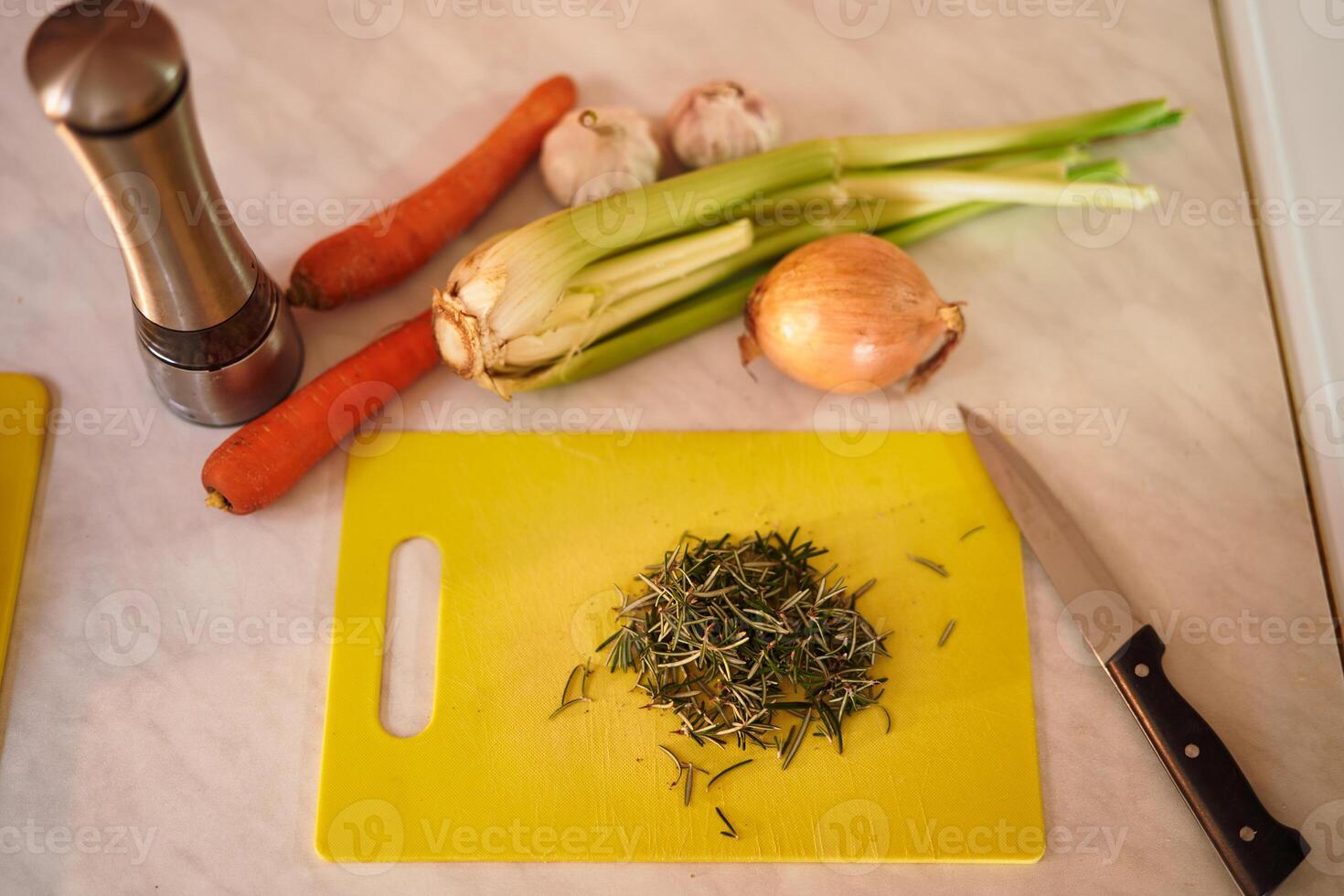 Chopped rosemary on a cutting board lies on the table next to vegetables photo
