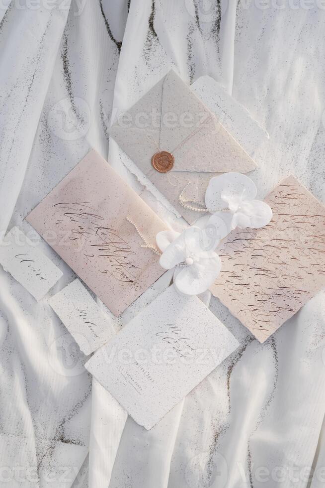 Wedding invitations with name cards lie next to envelopes and boutonnieres with beads on white fabric photo