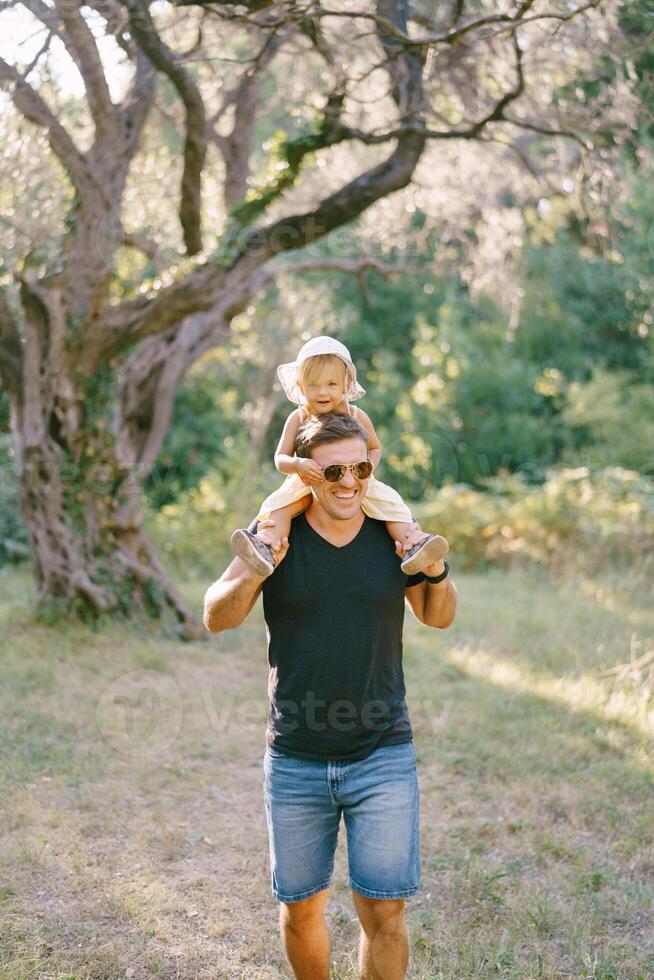 Little girl tugs sunglasses on dad face while sitting on his shoulders photo