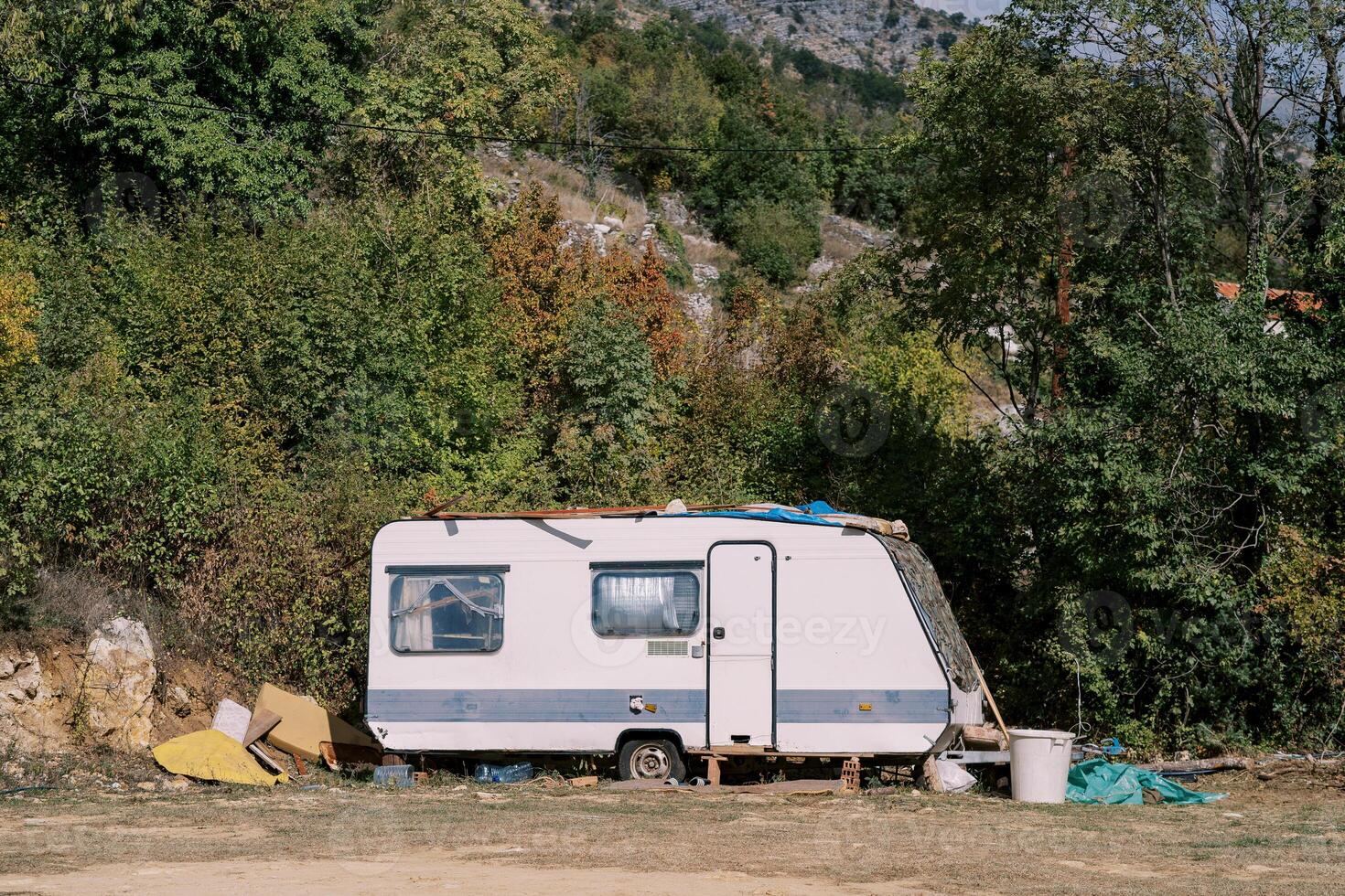 White camping car stands in a green forest at the foot of the mountains photo
