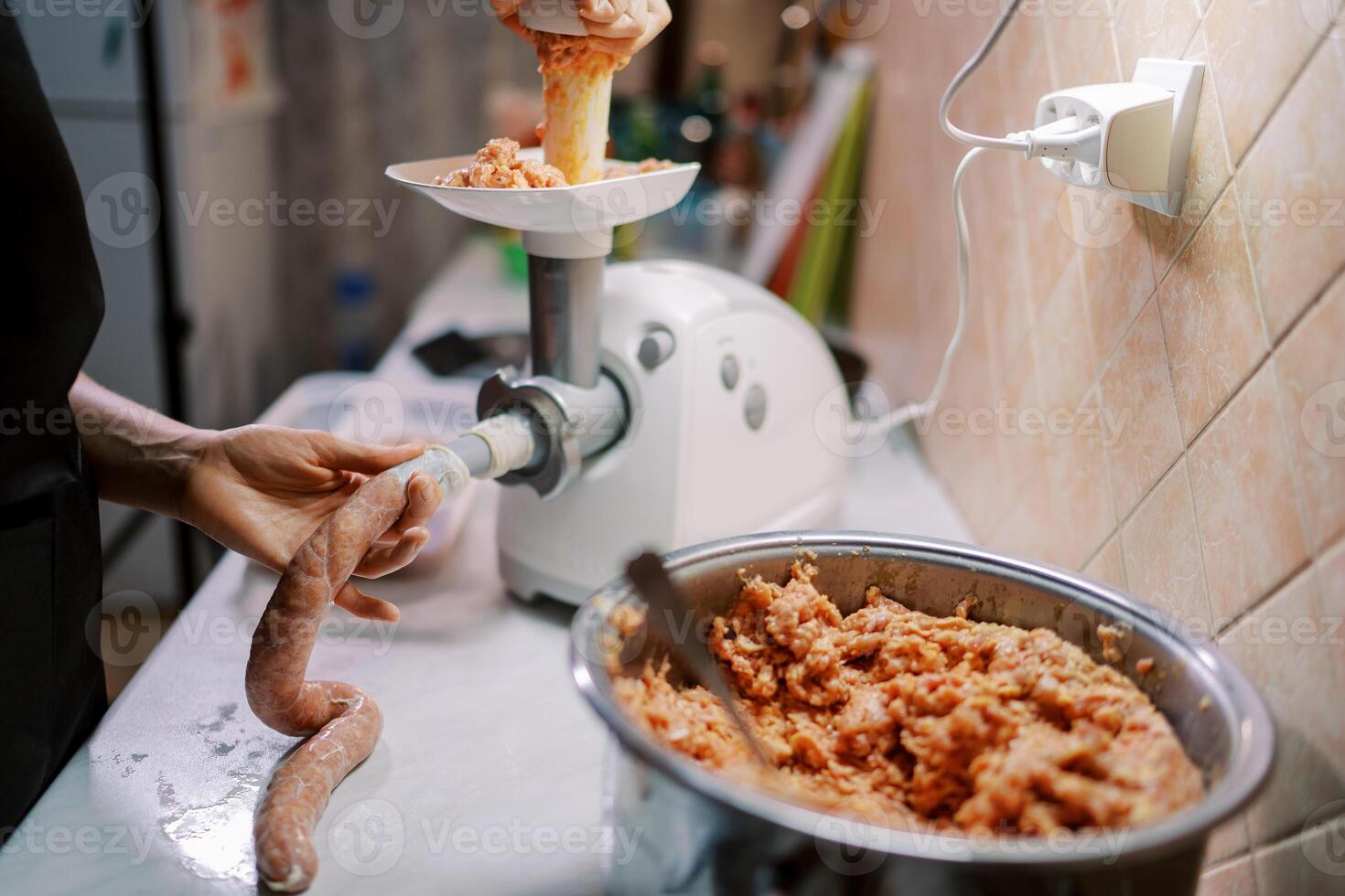 Housewife fills the intestine with minced meat in a meat grinder pushing it in the tray with a pusher photo