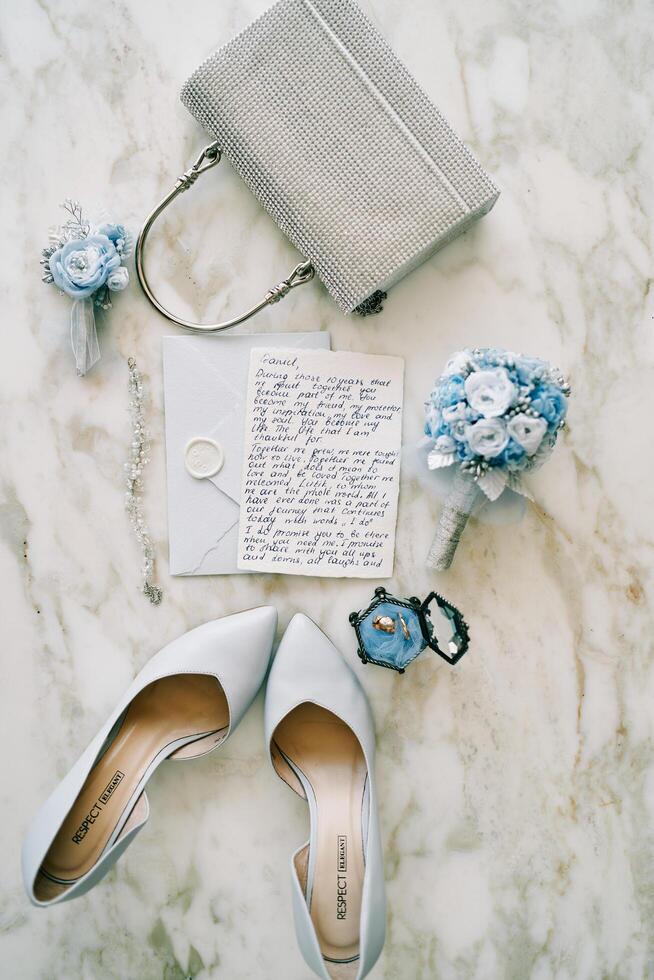 Montenegro, Budva - July 01, 2024. Bride shoes stand on a marble table near the wedding vow, a bouquet of flowers and a purse. Top view photo