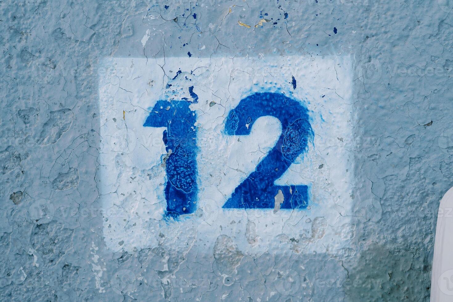 Drawn number twelve in a white rectangle on a blue peeling wall photo