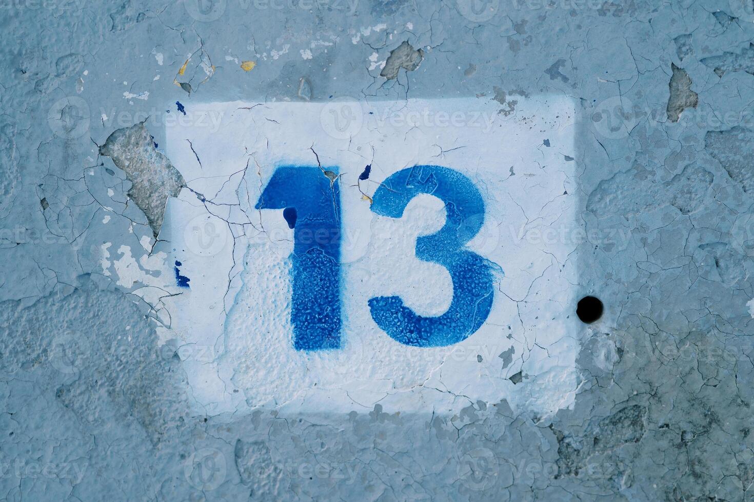 Number thirteen drawn in a white rectangle on a blue peeling wall photo