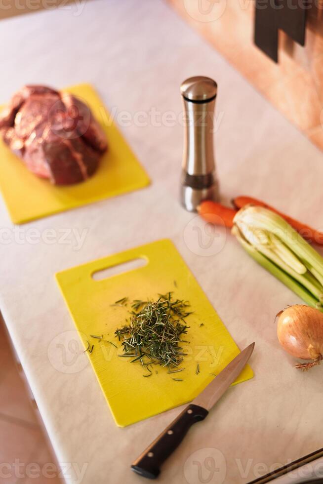 Finely chopped rosemary on a cutting board lies on the table next to raw tenderloin and vegetables photo