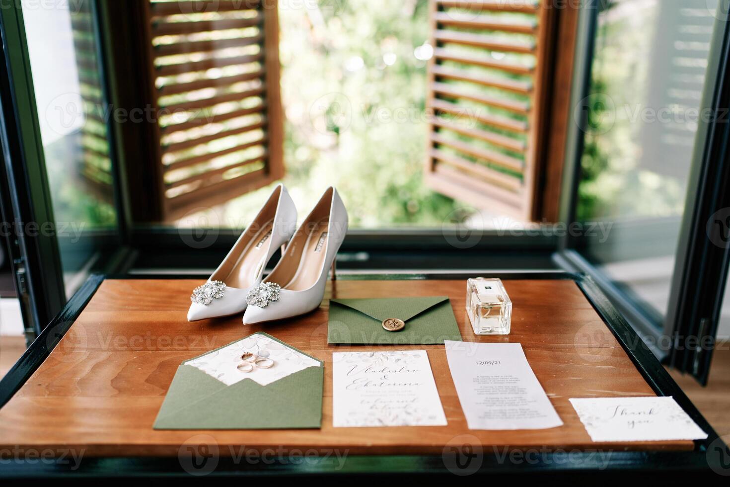 Bride shoes stand on a wooden table next to invitations in green envelopes near the window photo