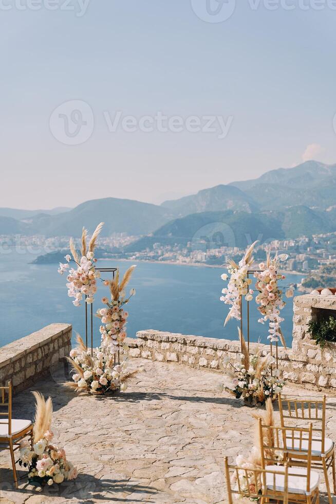 Chairs stand in front of a wedding semi-arch on an observation deck over the sea photo