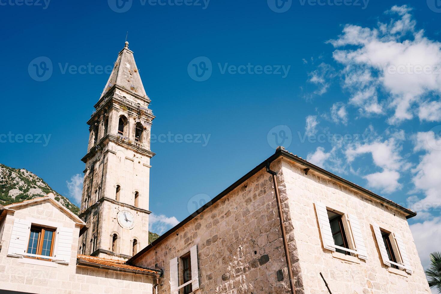 Old stone house with white shutters and an attic against the backdrop of the bell tower of the Church of St. Nicholas. Perast, Montenegro photo